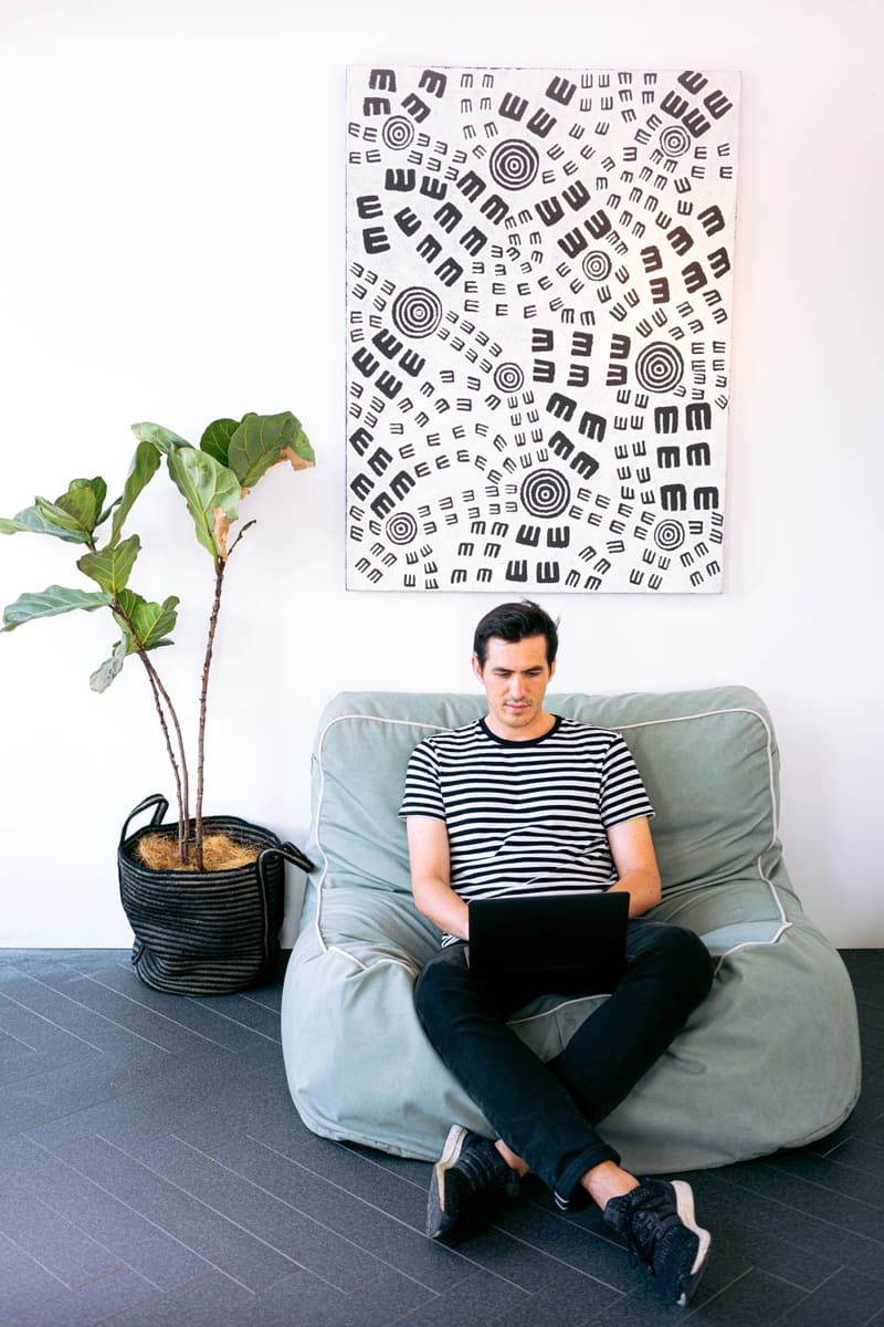 A student working on a laptop while seated on a floor cushion in a bright room