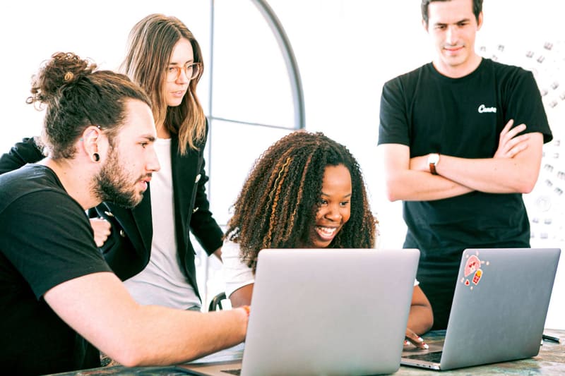 Students and a mentor gathered around laptops, smiling during a working session